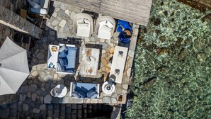 An outdoor patio with stone flooring, multiple seating areas, and a view of clear water.