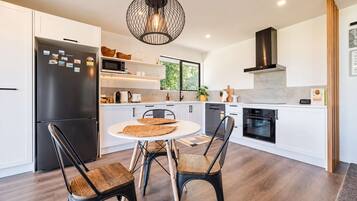 A modern kitchen with white cabinetry, a black refrigerator, a round dining table with two chairs, and a hanging light fixture.
