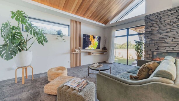 A modern living room with a stone fireplace, large windows, and a potted monstera plant.