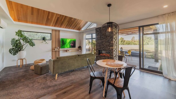 Ein modernes Wohnzimmer mit Kamin aus Stein, einem Fernseher und einem Essbereich mit Stühlen und Tisch.