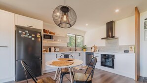 A modern kitchen with white cabinets, a black refrigerator, a round dining table with two chairs, and a hanging light fixture.