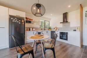Una cocina moderna con armarios blancos, un refrigerador negro, una mesa redonda de comedor con dos sillas y una lámpara colgante.