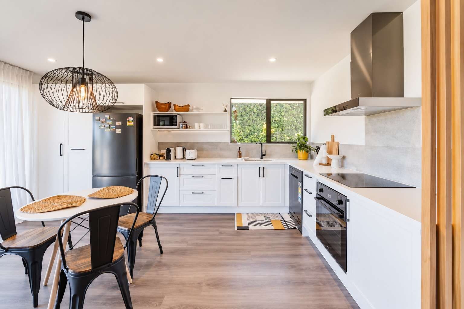 A modern kitchen with white cabinetry, a black refrigerator, and a dining area with a round table and chairs.