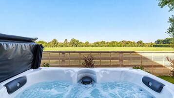 A hot tub with a wooden deck and a view of a green field.