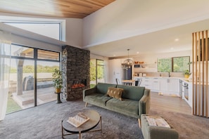 Amplia sala de estar con chimenea de piedra, un sofá verde y una mesa de comedor.