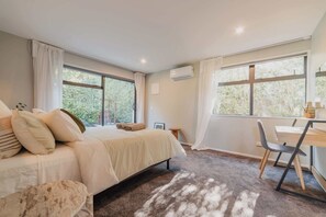 Un dormitorio con una cama, un escritorio y una silla. Hay ventanas y un equipo de aire acondicionado.