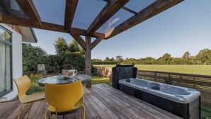 A wooden deck with a glass ceiling, a round table, yellow chairs, and a hot tub.