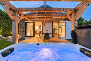 Un bain à remous sous une pergola en bois, avec vue sur une maison moderne et un espace patio.