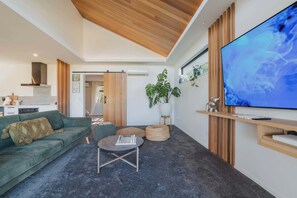Un salon moderne avec un canapé vert, une table basse ronde et un téléviseur à écran plat fixé au mur.