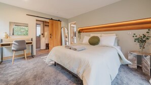 A bedroom with a bed, a desk, and a chair. There is a window with a view of greenery.