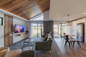 Una sala de estar moderna con chimenea de piedra, techo de madera y un televisor grande.