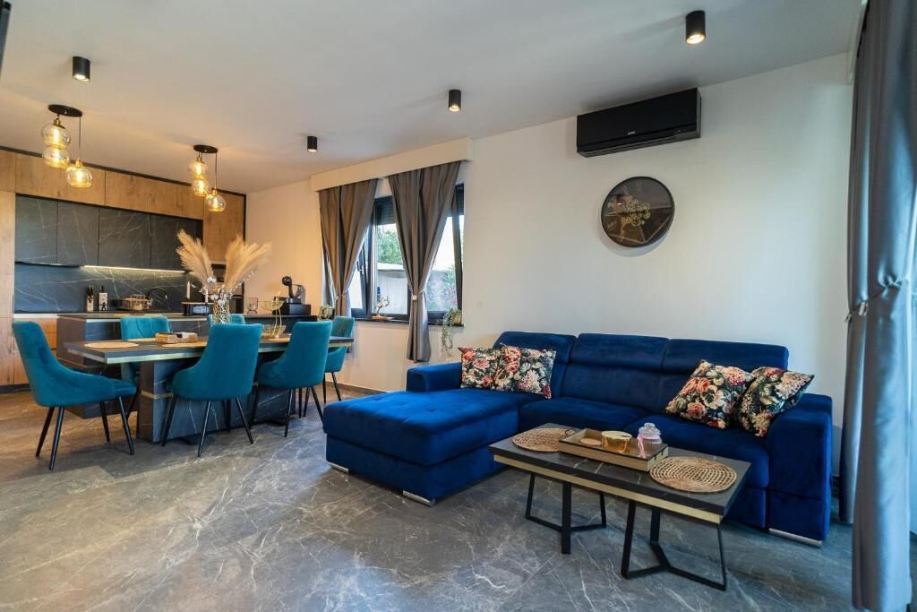 A modern living room with a blue sofa, a dining area with blue chairs, and a kitchen in the background.