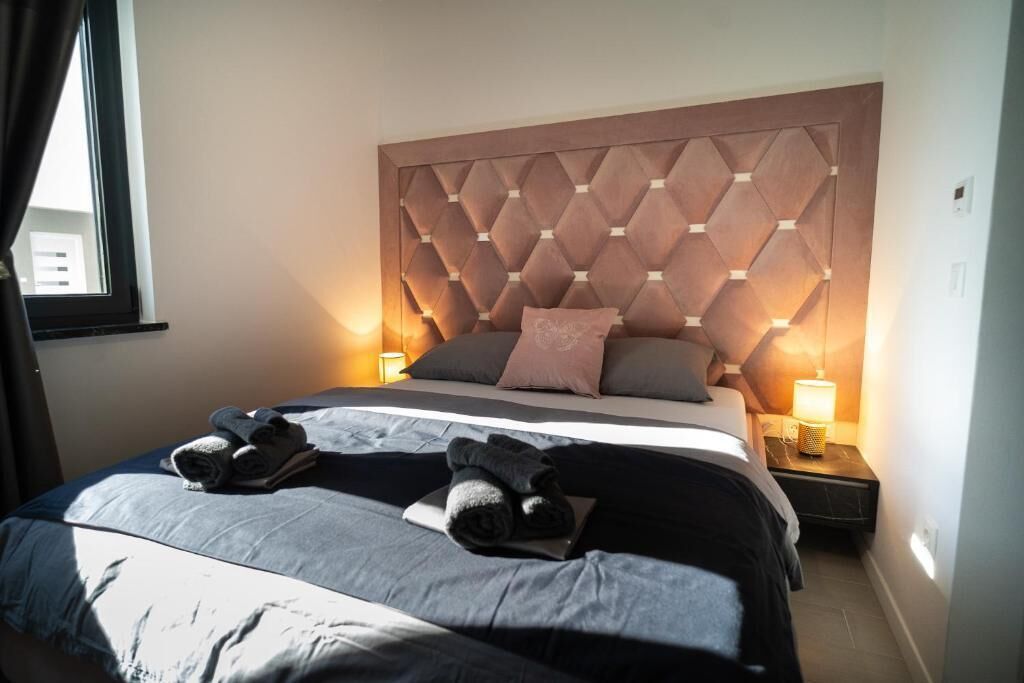 Un lit bien fait, avec une tête de lit, deux lampes de chevet et des serviettes pliées posées sur le lit.