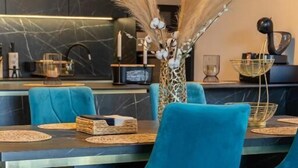 A modern dining area with teal chairs, a marble table, and decorative elements like pampas grass and a vase with white flowers. - La Vista Azure (Sukosan)