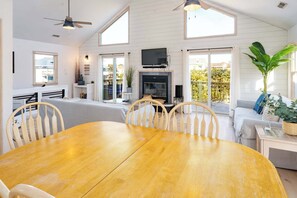 A spacious room with a wooden dining table, white walls, and large windows offering views of the outdoors. - Oceanside with Pool Hot Tub and Updated Interior! (Corolla)
