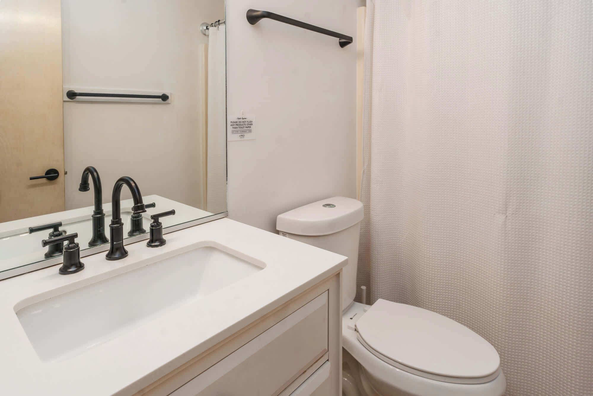 Un baño con lavamanos blanco, grifos negros, inodoro blanco y cortina de ducha.