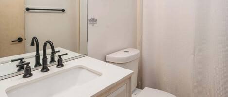 Un baño con lavamanos blanco, grifos negros, inodoro blanco y cortina de ducha.