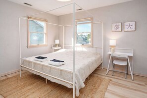 A four-poster bed with a white canopy, two bedside tables with lamps, a small desk with a chair, and two framed pictures on the wall. - Oceanside with Pool Hot Tub and Updated Interior! (Corolla)