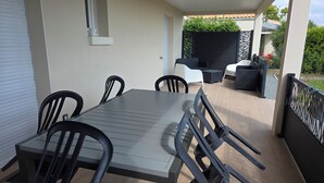 A covered patio with a table and chairs, a small seating area with a sofa and chairs, and a decorative fence.
