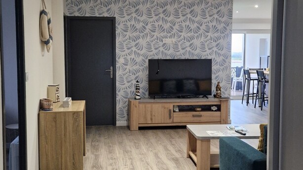 A modern living room with a flat-screen TV, wooden furniture, and patterned wallpaper.