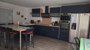 A modern kitchen with dark blue cabinets, a stainless steel refrigerator, a built-in oven, and a coffee maker.