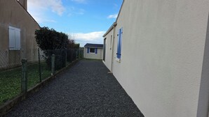 A narrow gravel path between buildings with chain-link fences and a clear blue sky.
