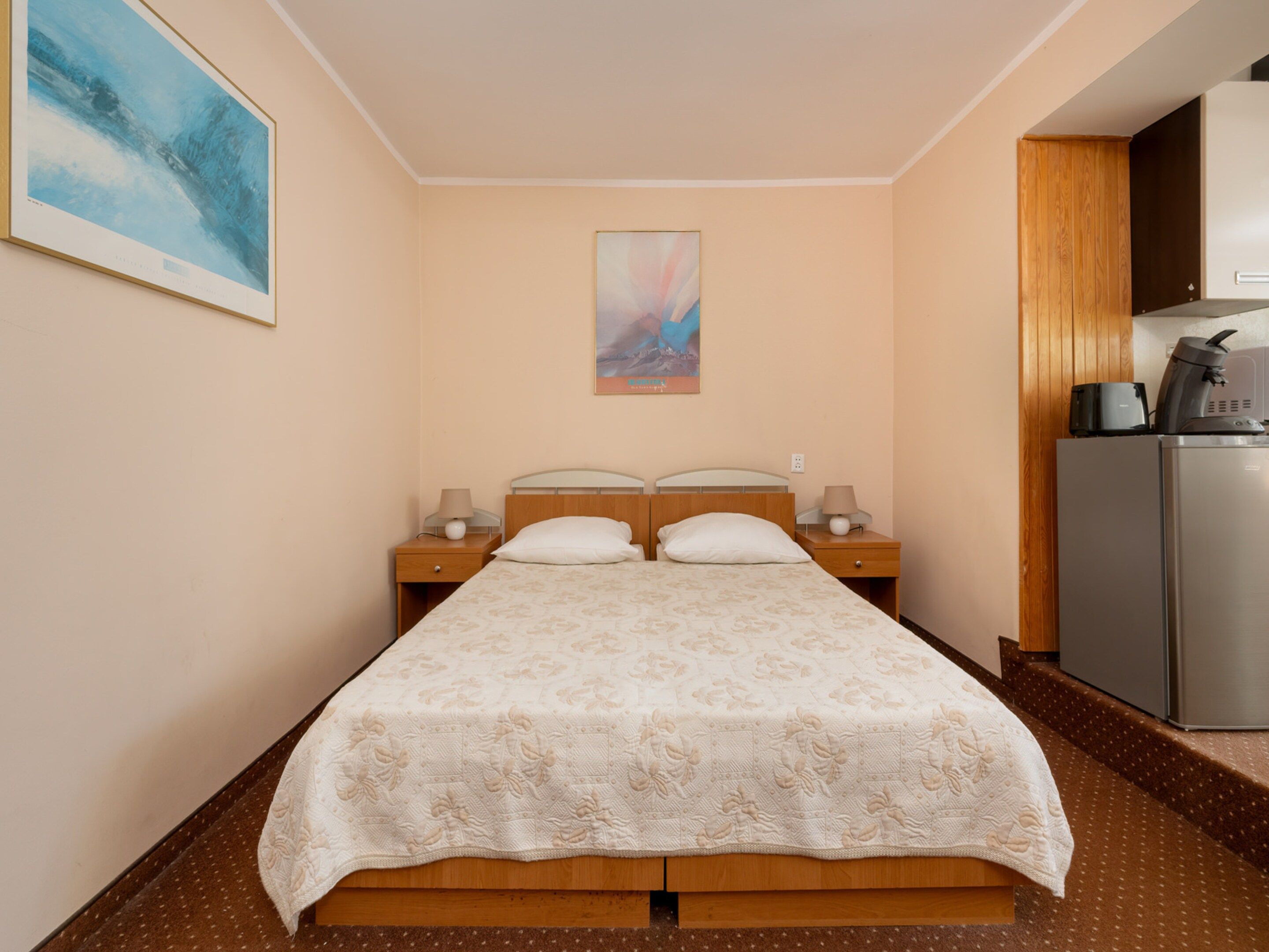 A hotel room with a bed, two bedside tables, a coffee machine, and artwork on the walls.