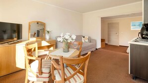 Habitación de hotel compacta con zona de comedor, sofá, televisión y kitchenette.