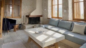 A rustic room with a stone wall, wooden beams, a fireplace, a sofa, and a table. - Pervola Private Stone Estate | 5 acres Exclusive Grove and Pool (gazion)