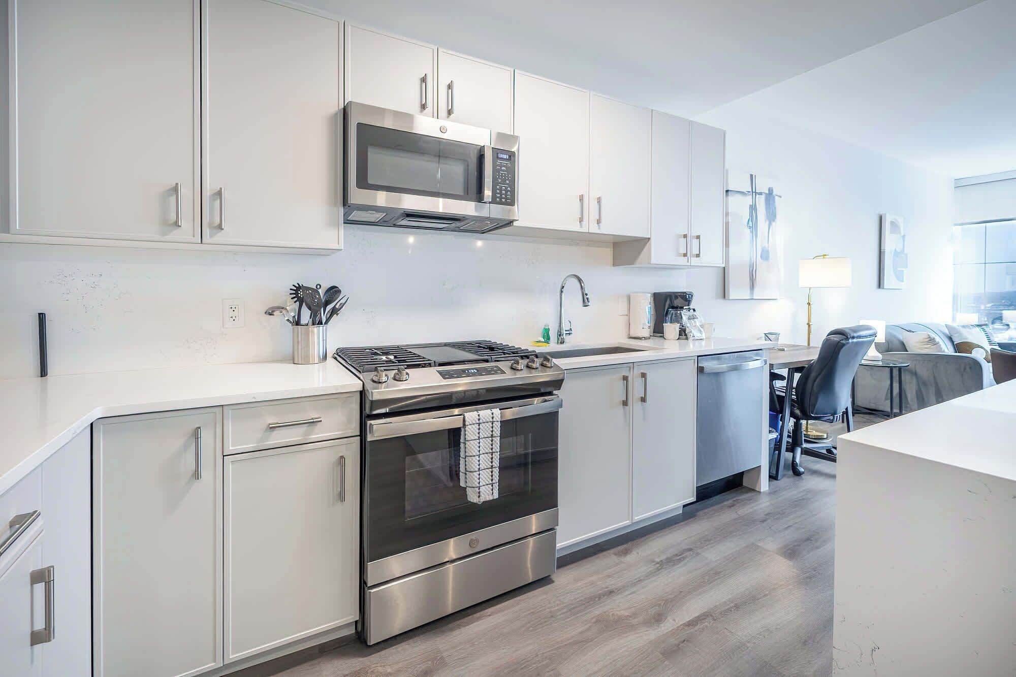 A modern kitchen with stainless steel appliances, white cabinetry, and a grey floor.