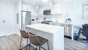 A modern kitchen with white cabinetry, stainless steel appliances, and a central island with bar stools. - Luxury Modern Apt with Pool (Stamford, CT)