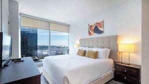 A hotel room with a large bed, a desk, a TV, and a city view. - Luxury Modern Apt with Pool (Stamford, CT)