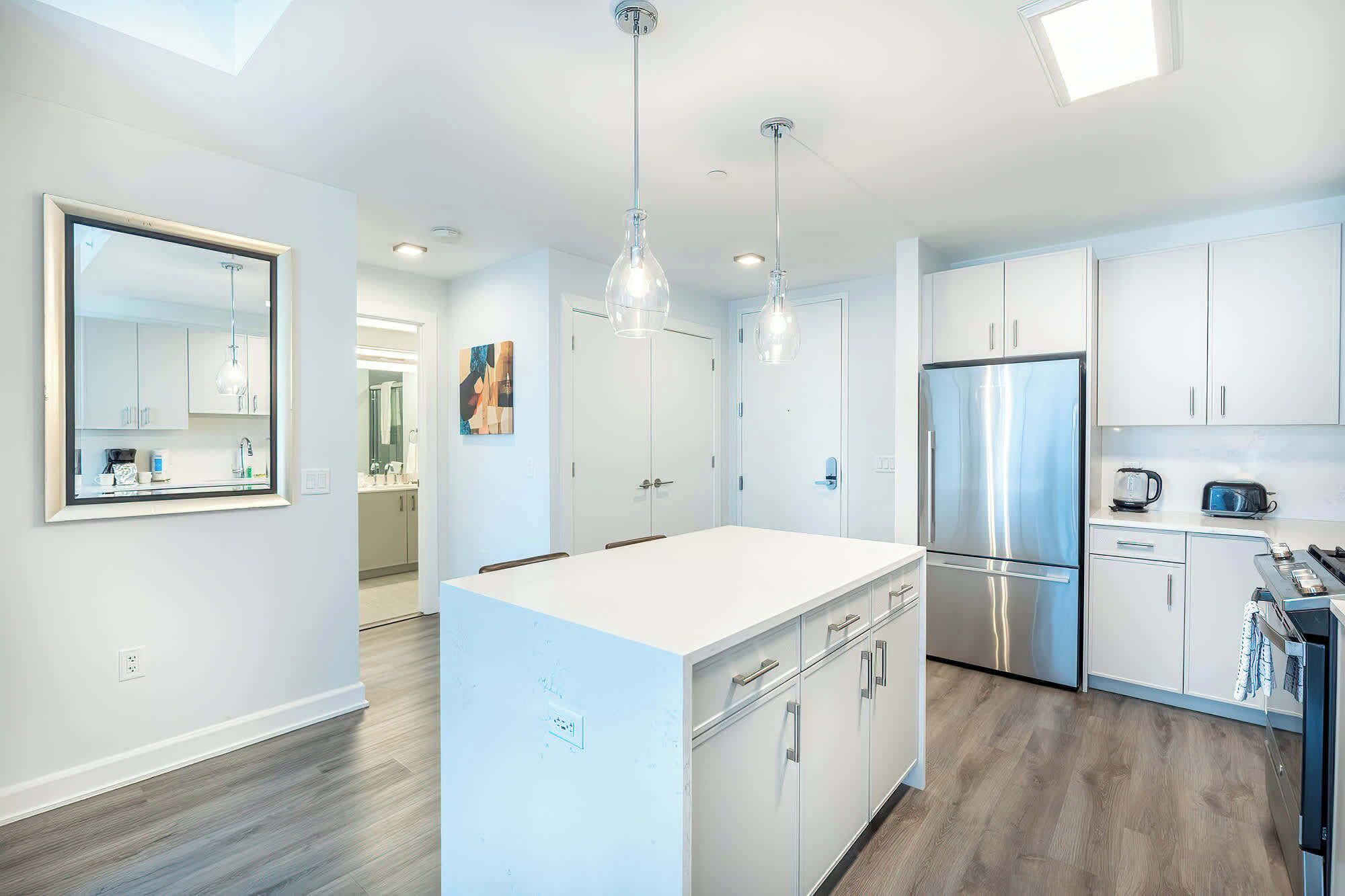 Una cocina moderna con gabinetes blancos, un refrigerador de acero inoxidable, luces colgantes y una isla grande con un lavamanos.