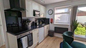 Une cuisine compacte équipée d’un four à micro-ondes, d’un four et d’un évier. Il y a une horloge au mur et une fenêtre donnant sur l’extérieur.