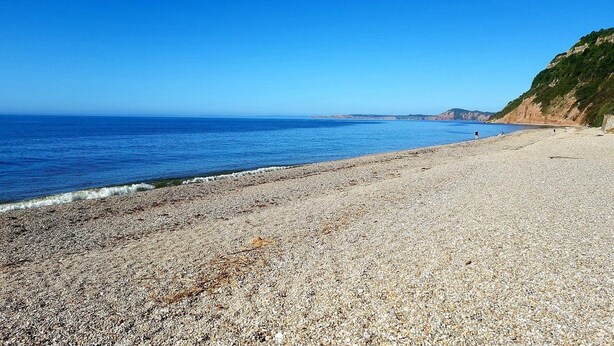 Une plage de galets, avec un ciel bleu clair et une mer calme.