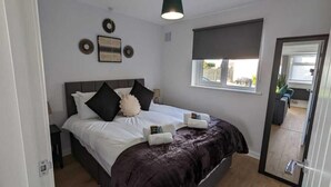 Une chambre à coucher comprenant un lit, des oreillers, une table de chevet, une fenêtre donnant sur un paysage agréable et une porte menant à une autre pièce.