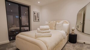 A bedroom with a large bed, a side table, a mirror, and a view of the city through a sliding door. - Bianco Suite 2BR with City Views (Greater Manchester)