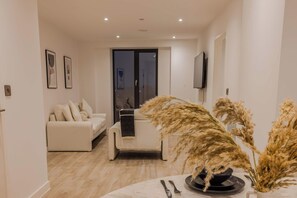 Een moderne woonkamer met een bank, een eettafel met bestek en een vaas gedroogde planten.
