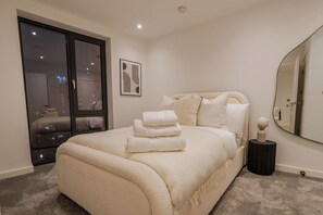 Ein Schlafzimmer mit einem großen Bett, einem Nachttisch, einem Spiegel und Blick auf die Stadt durch eine Schiebetür.