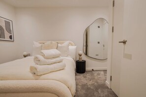 Een slaapkamer met een bed, een ronde spiegel en een deur.