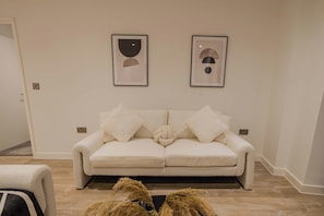 A modern living room with a beige sofa, two framed abstract artworks, and a fluffy rug. - Bianco Suite 2BR with City Views (Greater Manchester)