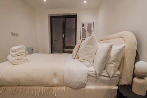 A neatly made bed with a folded towel, a bedside table with a lamp, and a door leading to a bathroom.