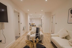 A modern living room with a sofa, a coffee table with decorative plants, and a flat-screen TV mounted on the wall.