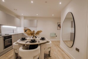 Een moderne keuken met witte kastjes, een ronde eettafel met witte stoelen en een grote spiegel aan de muur.