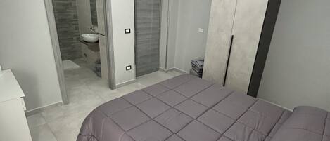 Un dormitorio moderno con una cama grande, un armario y un baño visible a través de una puerta abierta.