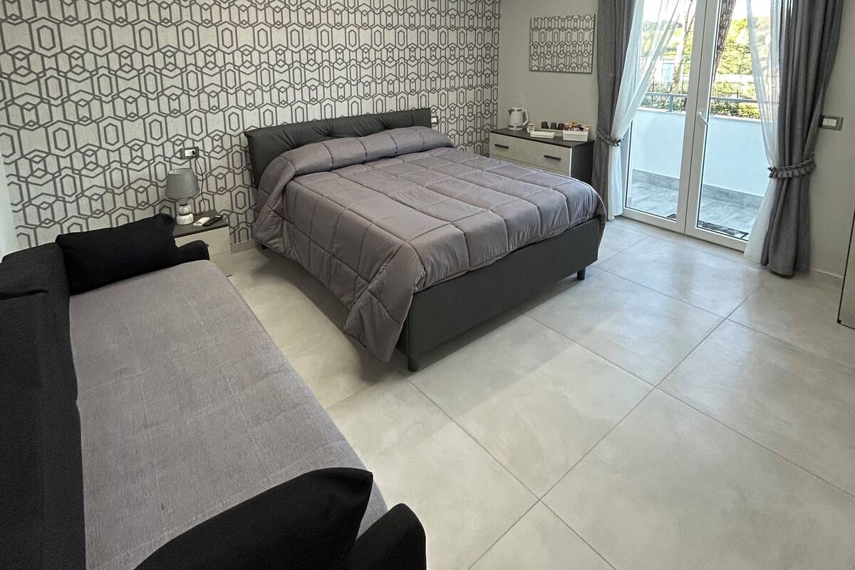 A modern bedroom with a large bed, a sofa, and a balcony with curtains.