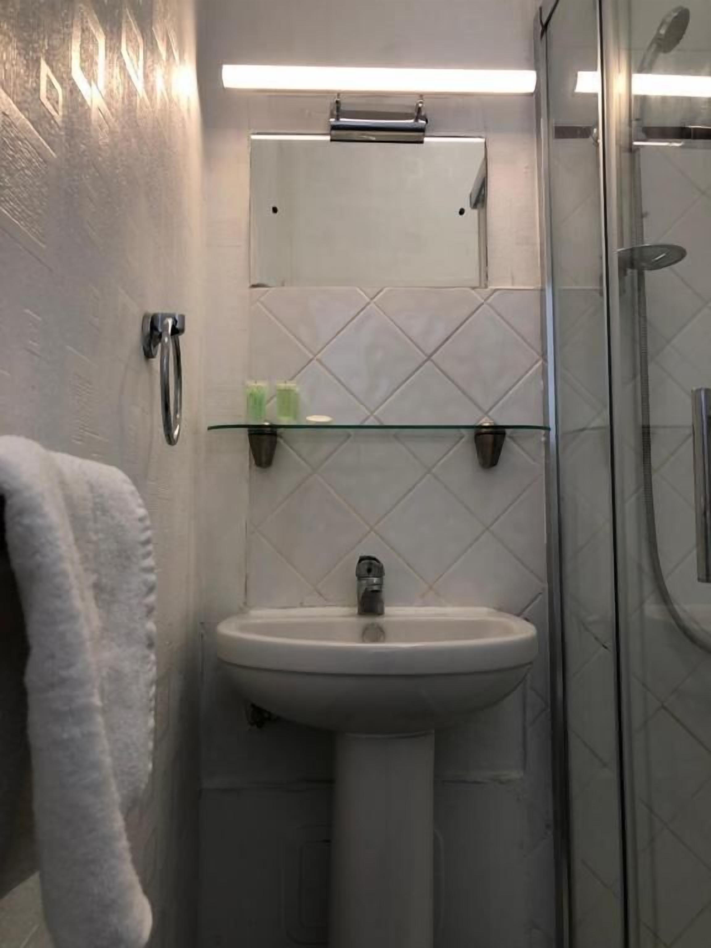 A bathroom with a glass shower enclosure, a white sink with a mirror above it, and a towel hanging on the wall.