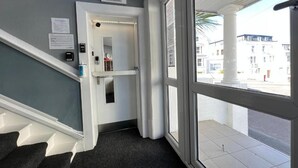 Ein Empfangsbereich mit Schilder, Kleiderhaken, einem Feuerlöscher und einem Fenster mit Blick auf Gebäude.