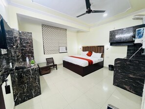 A hotel room with a bed, a desk, a chair, a ceiling fan, and a TV mounted on the wall. - Hotel Silver Stay 04 (Jaipur)