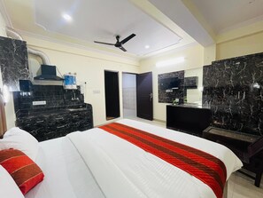 A hotel room with a bed, a desk, a TV, a ceiling fan, and a bathroom door. - Hotel Silver Stay 04 (Jaipur)